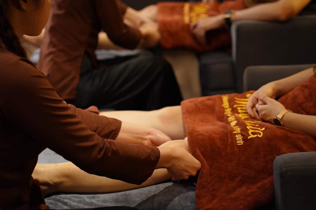 Nhân viên massage chân cho khách tại spa. Không gian thư giãn với chăn màu nâu sang trọng.