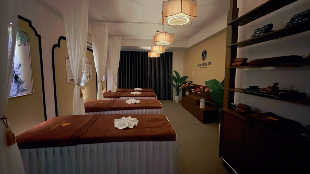 Phòng spa yên tĩnh với giường massage sắp xếp gọn gàng, trang trí nến và rèm trắng nhẹ nhàng.