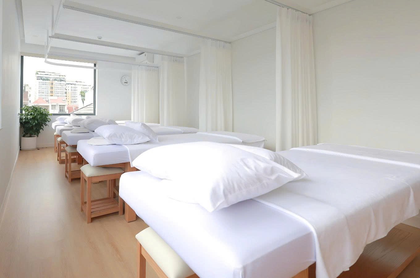 Phòng spa hiện đại với giường massage xếp hàng, ánh sáng tự nhiên, không gian sạch sẽ và sang trọng.