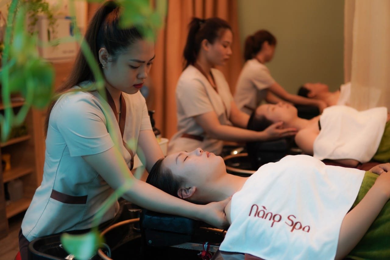 Nhân viên spa massage mặt cho khách hàng trong không gian thư giãn với cây xanh.