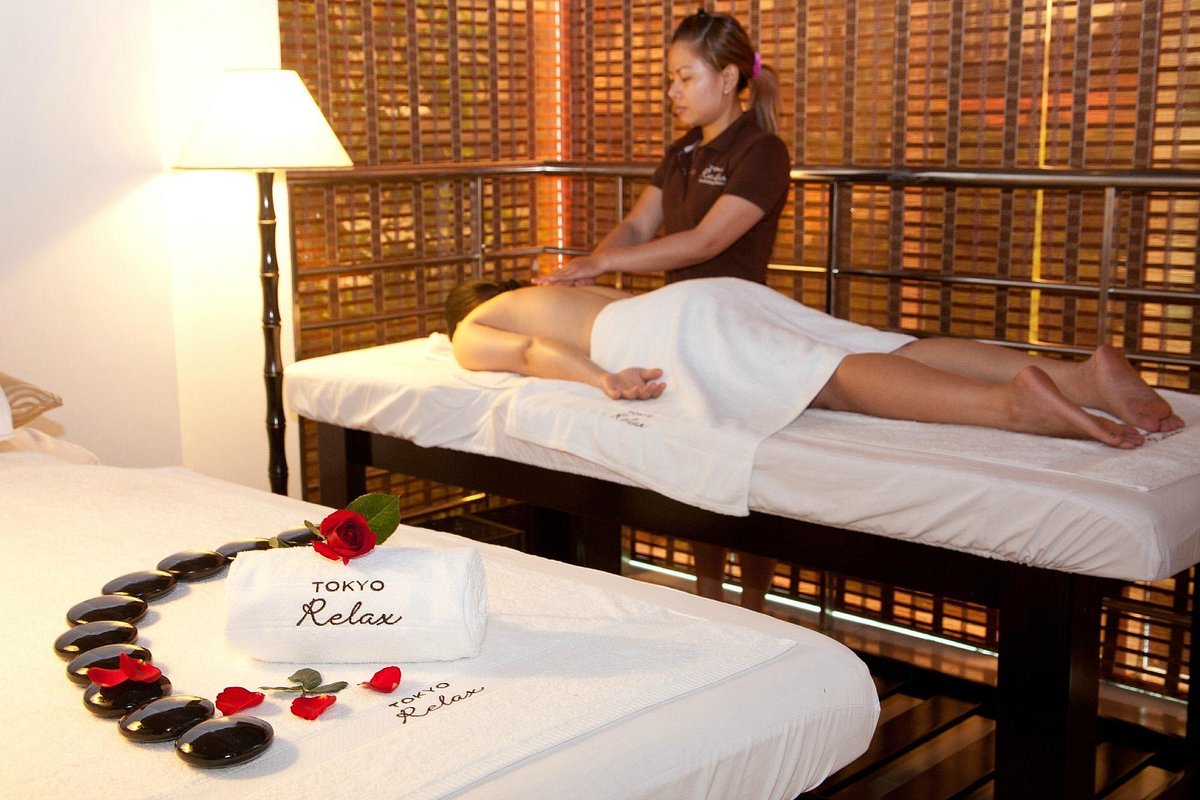 Nhân viên spa đang massage cho khách hàng trên giường, bên cạnh là khăn và đá nóng trang trí.