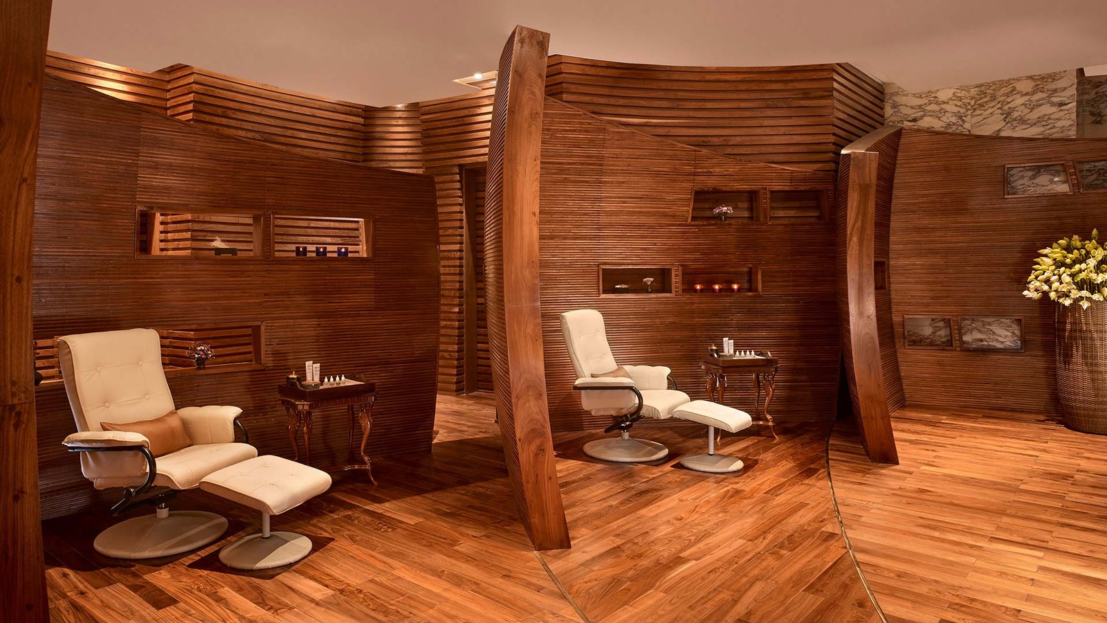 Nội thất spa sang trọng với ghế massage màu kem, bàn gỗ và vách ngăn gỗ ấm áp, tạo không gian thư giãn.