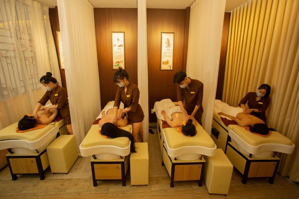 Nhân viên spa đang thực hiện massage cho khách hàng trên giường, không gian chia ngăn bằng rèm trắng.
