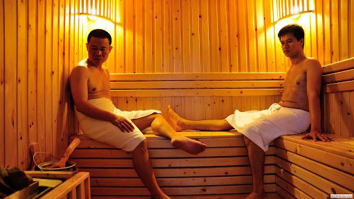 Hai người đàn ông trong phòng xông hơi gỗ sáng đèn thư giãn.