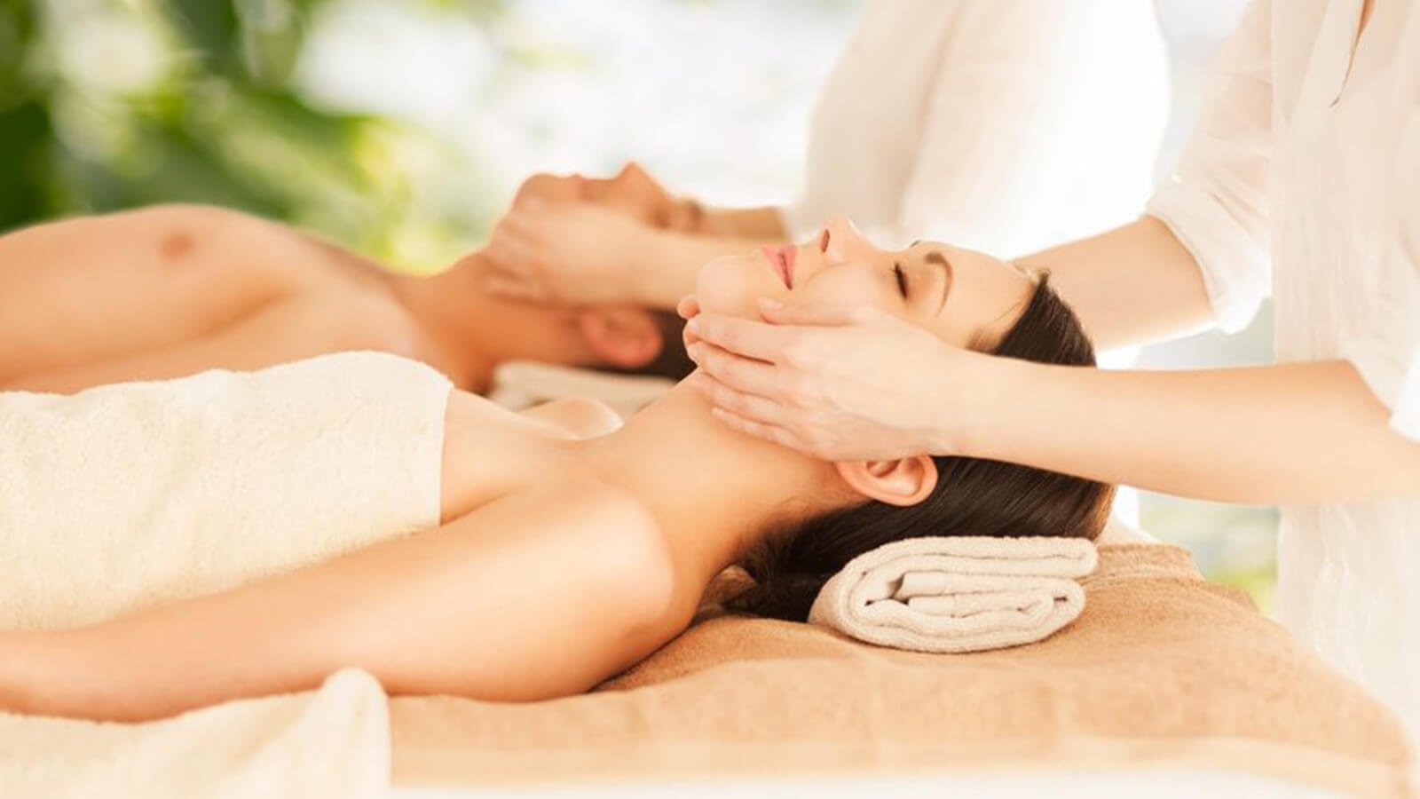Hai người đang thư giãn với liệu pháp mát-xa, nằm trên giường với khăn tắm, trong không gian spa yên tĩnh.