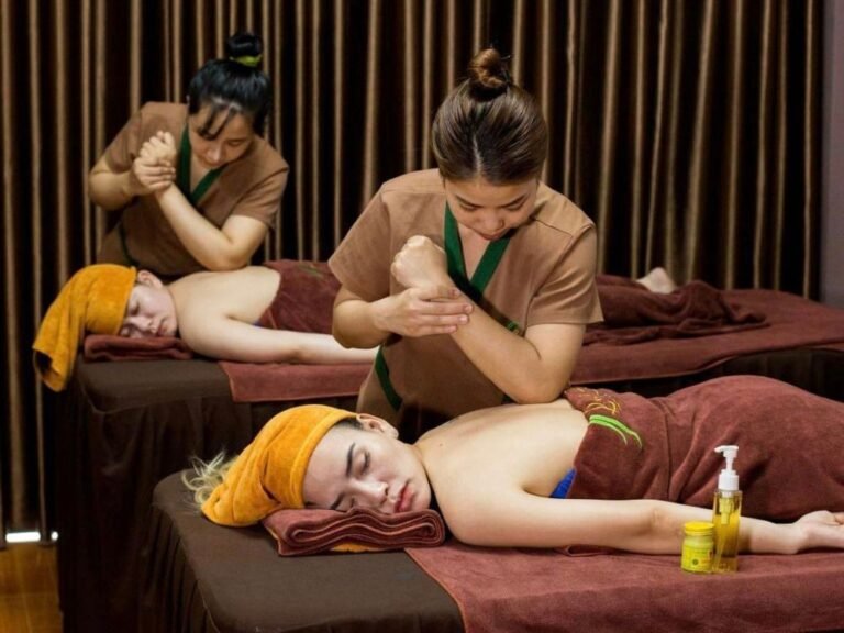 Hai người phụ nữ đang thư giãn và được mát-xa tại spa với khăn quấn cam nổi bật và không gian ấm cúng.