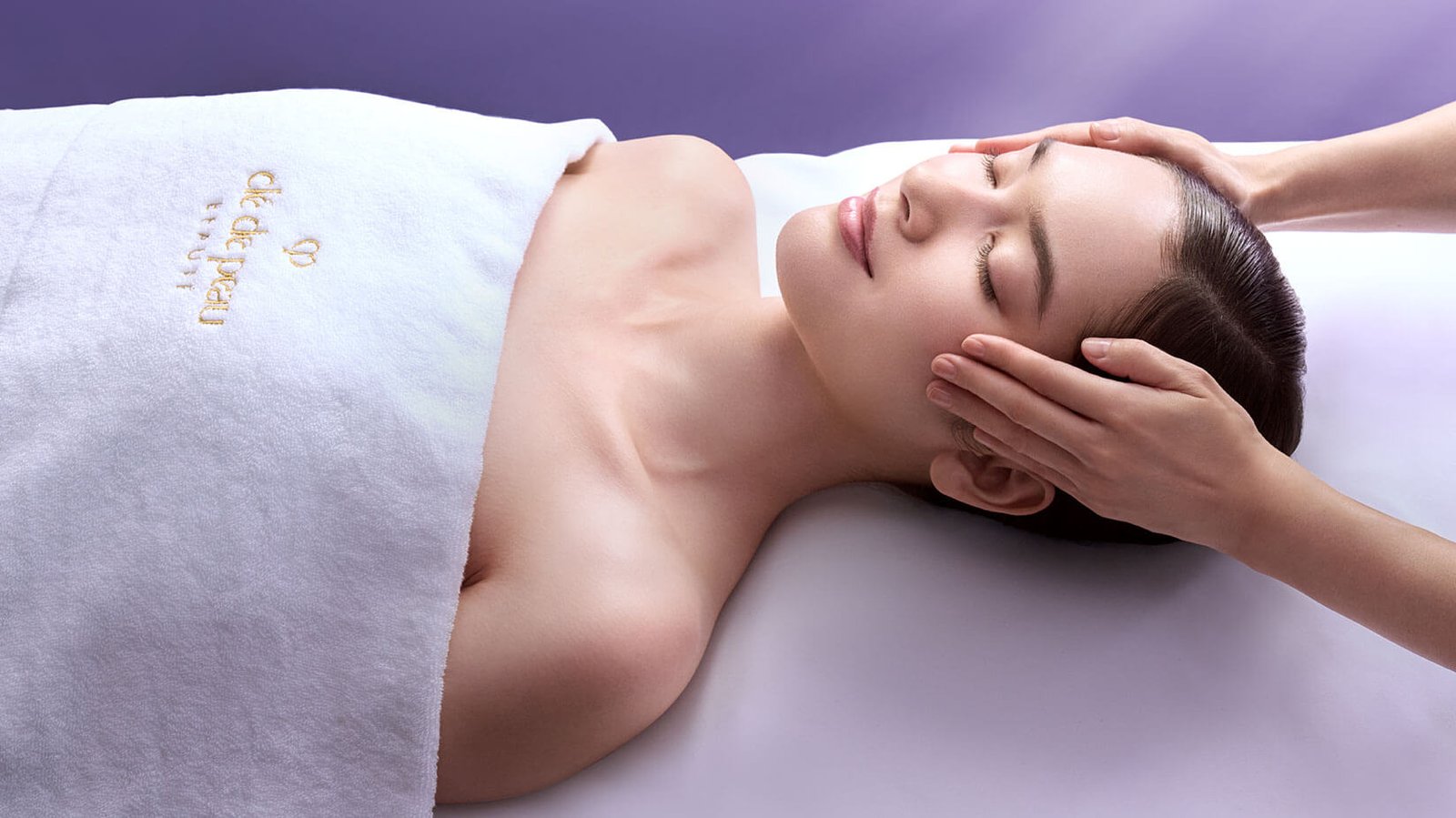 Người phụ nữ thư giãn trong phòng spa, nhận liệu pháp massage mặt, thoải mái dưới khăn mềm mại.