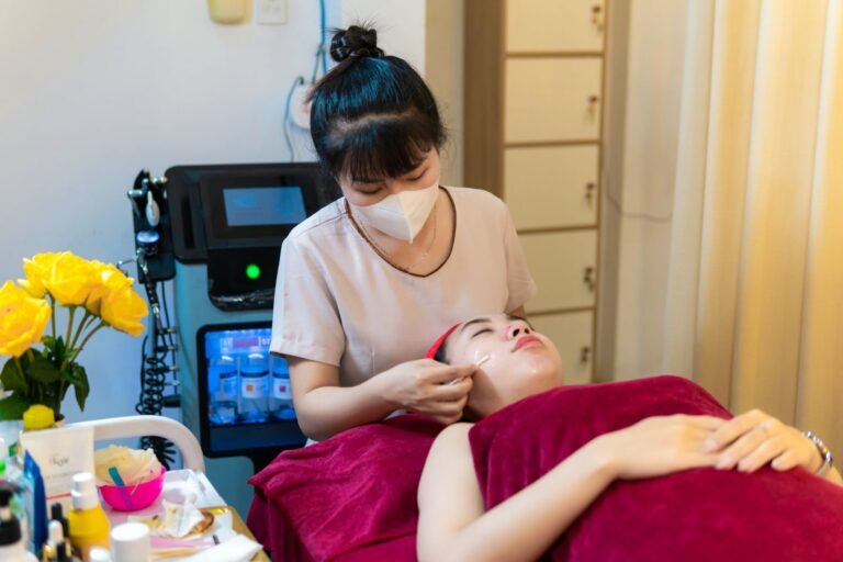 Nhân viên spa đang chăm sóc da mặt cho khách hàng trong không gian thư giãn với hoa vàng tươi.