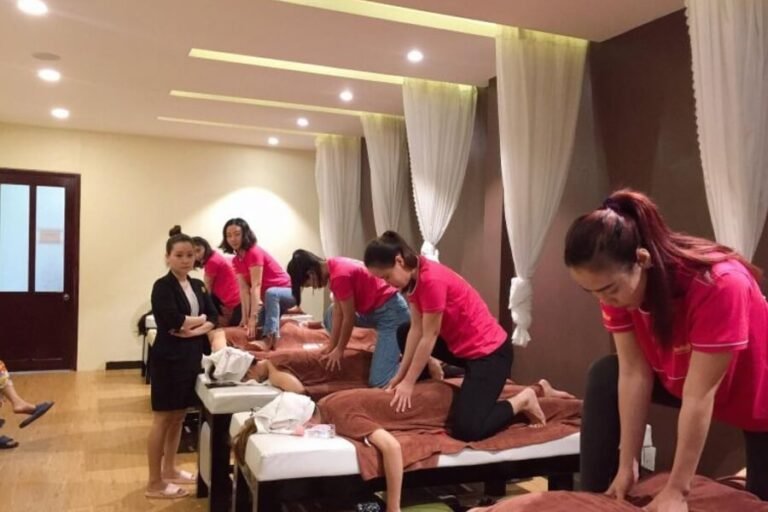 Nhân viên massage tại spa với áo thun hồng phục vụ khách hàng trên giường trị liệu.
