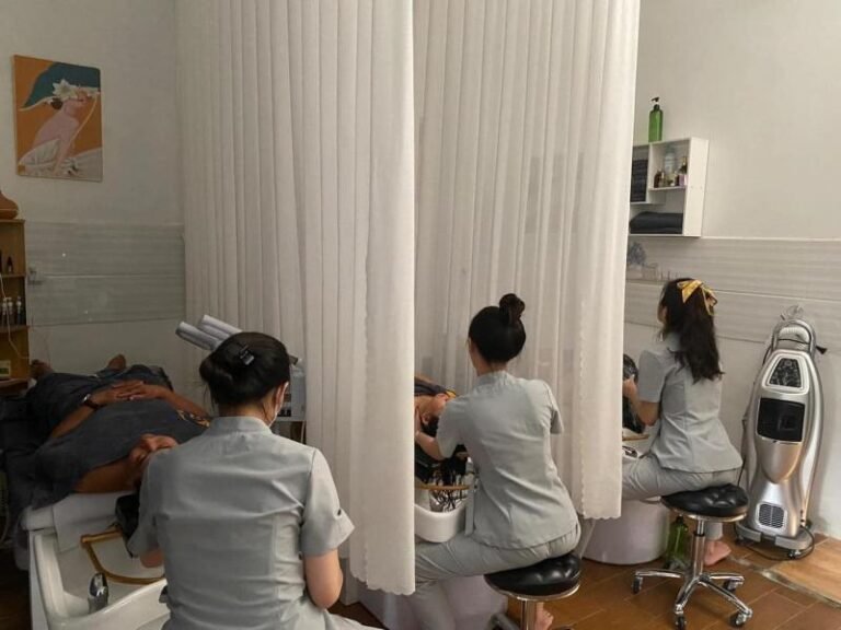 Nhân viên spa chăm sóc khách hàng trong phòng dịch vụ với màn che trắng, chăm sóc chuyên nghiệp và thư giãn.