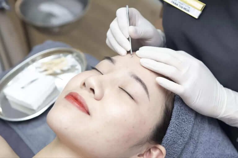 Chăm sóc da mặt tại spa, kỹ thuật viên đeo găng tay dùng nhíp làm sạch da mặt khách hàng.