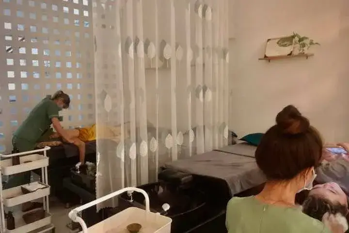 Nhân viên spa mát xa cho khách trong không gian thư giãn với rèm ngăn cách và trang trí cây xanh.