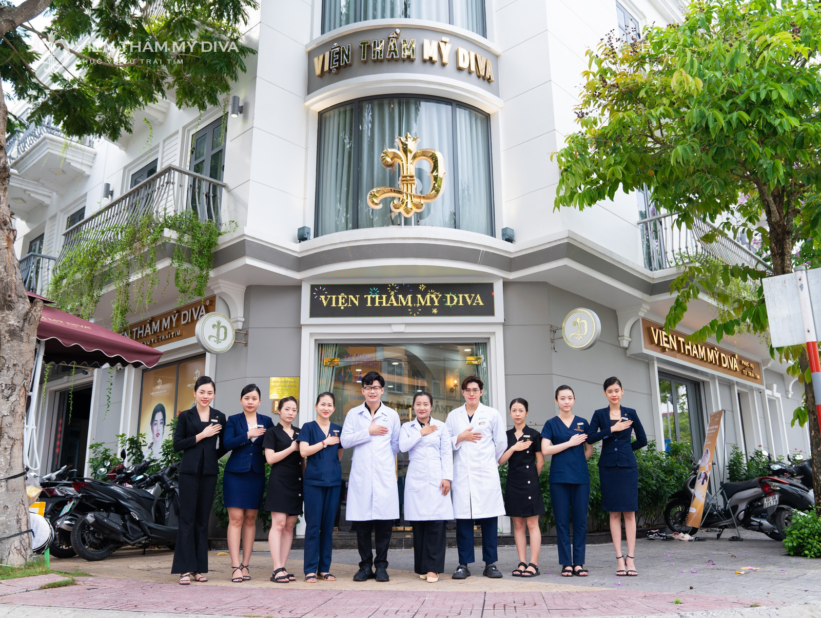 Nhóm nhân viên Viện thẩm mỹ Diva đứng trước cơ sở, mặc đồ công sở, tạo dáng chụp ảnh.