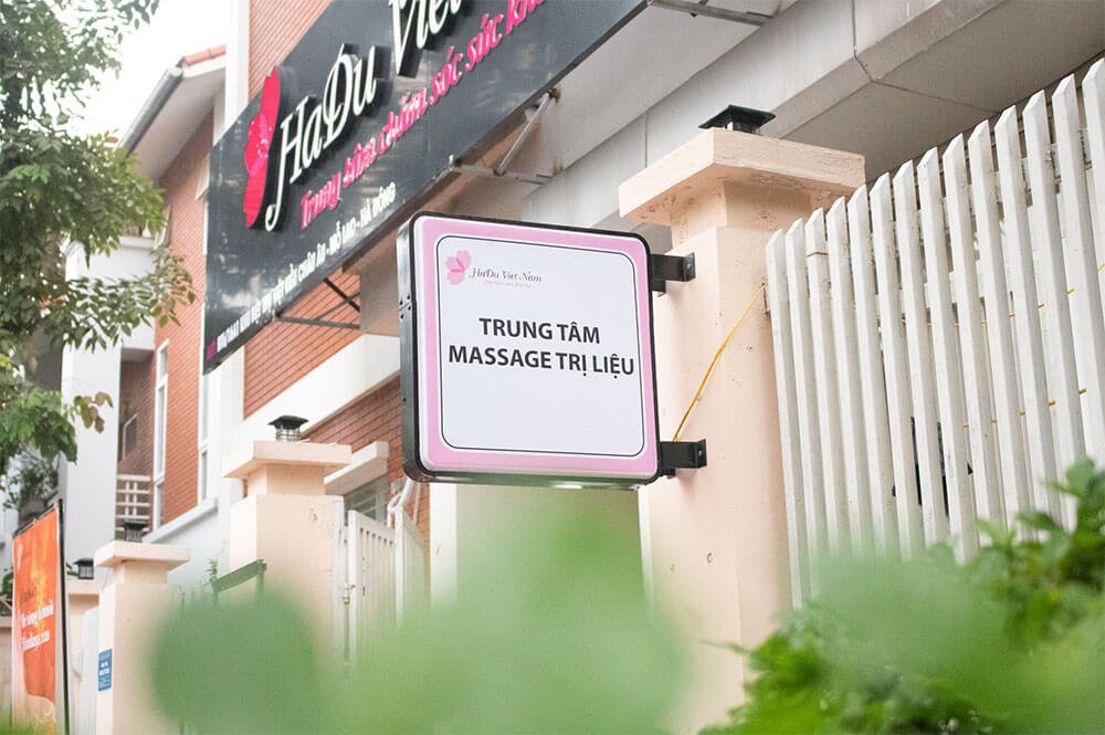 Biển hiệu trung tâm massage trị liệu bên ngoài tòa nhà, trang trí cây xanh phía trước.