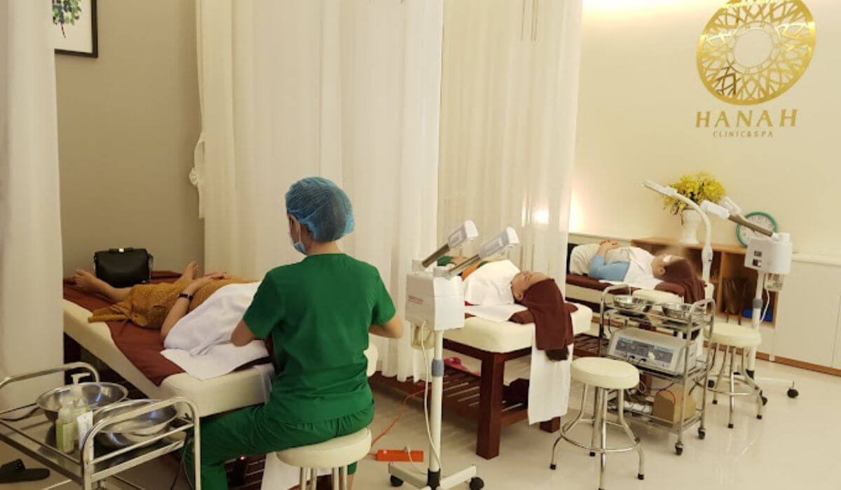 Phòng spa với nhiều giường, chuyên viên chăm sóc đang làm việc, thiết bị spa và trang trí nhẹ nhàng.
