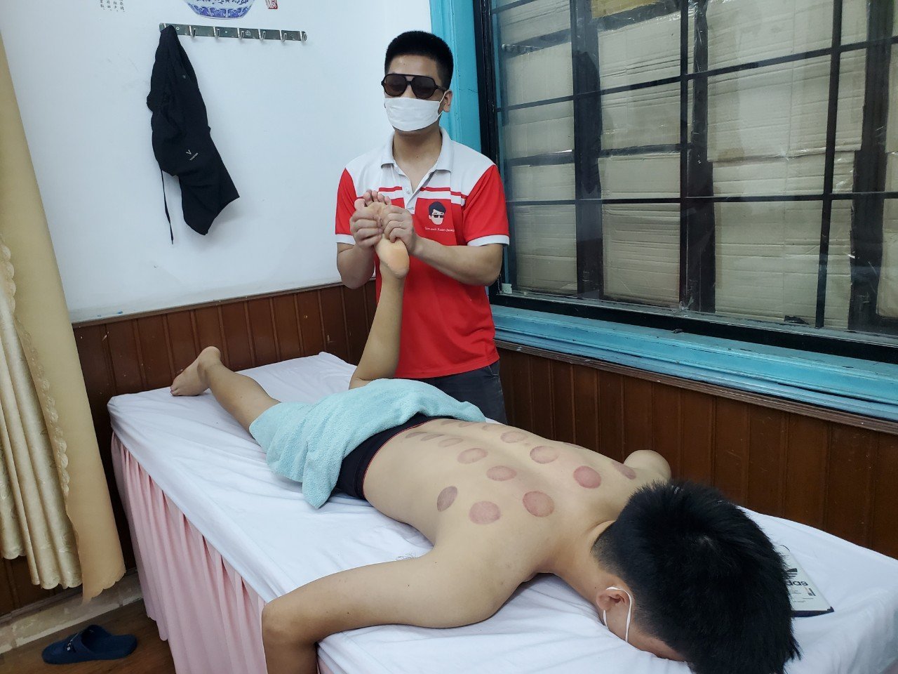 Người đàn ông massage chân cho người khác, với dấu giác hơi trên lưng tại một phòng trị liệu.