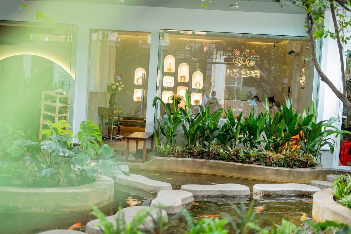 Mặt trước spa với cửa kính lớn, cây xanh và hồ cá tạo không gian thư giãn.
