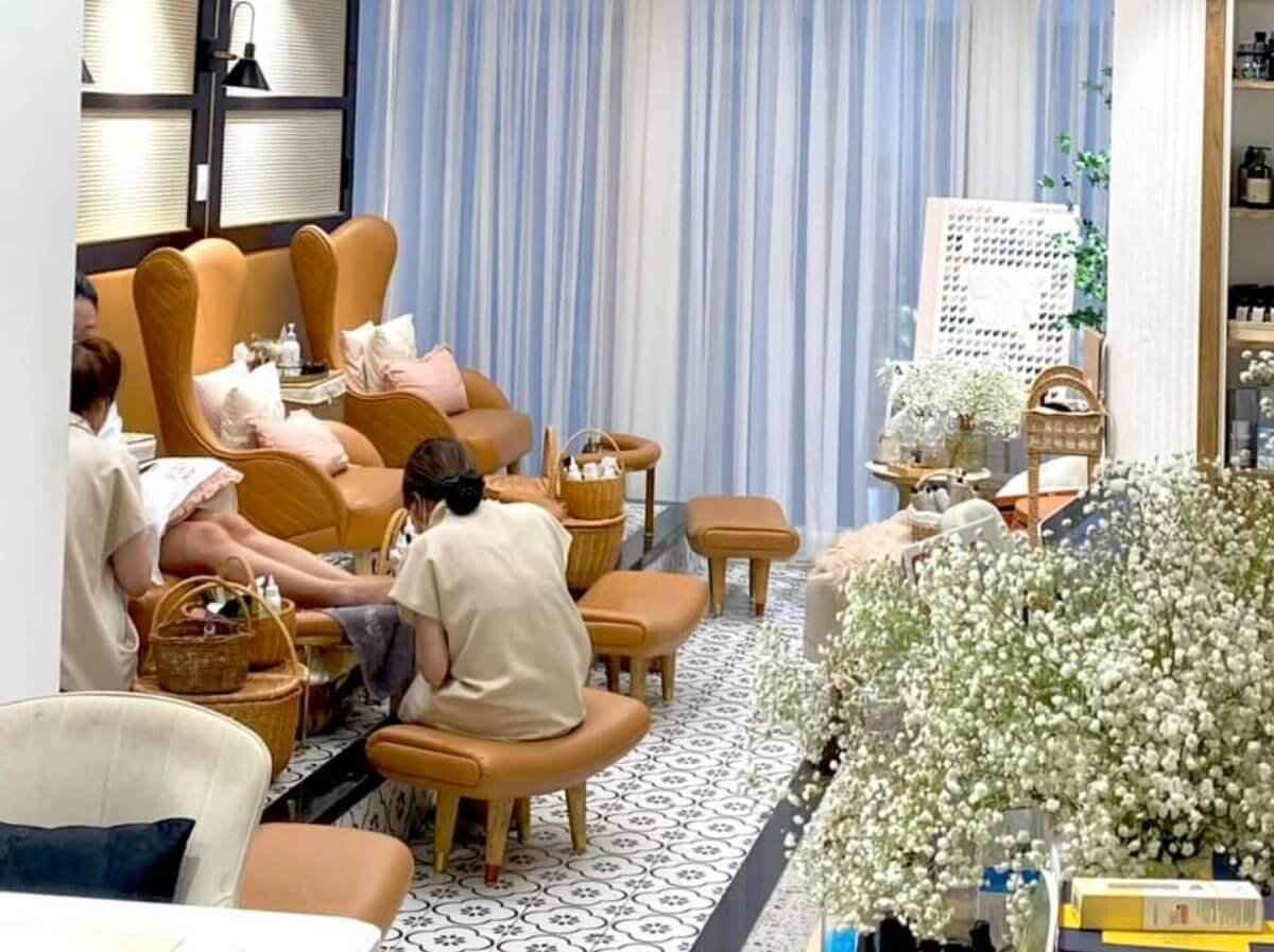 Tiệm spa làm móng với ghế da màu nâu, nhân viên chăm sóc khách hàng, không gian sang trọng và thư giãn.