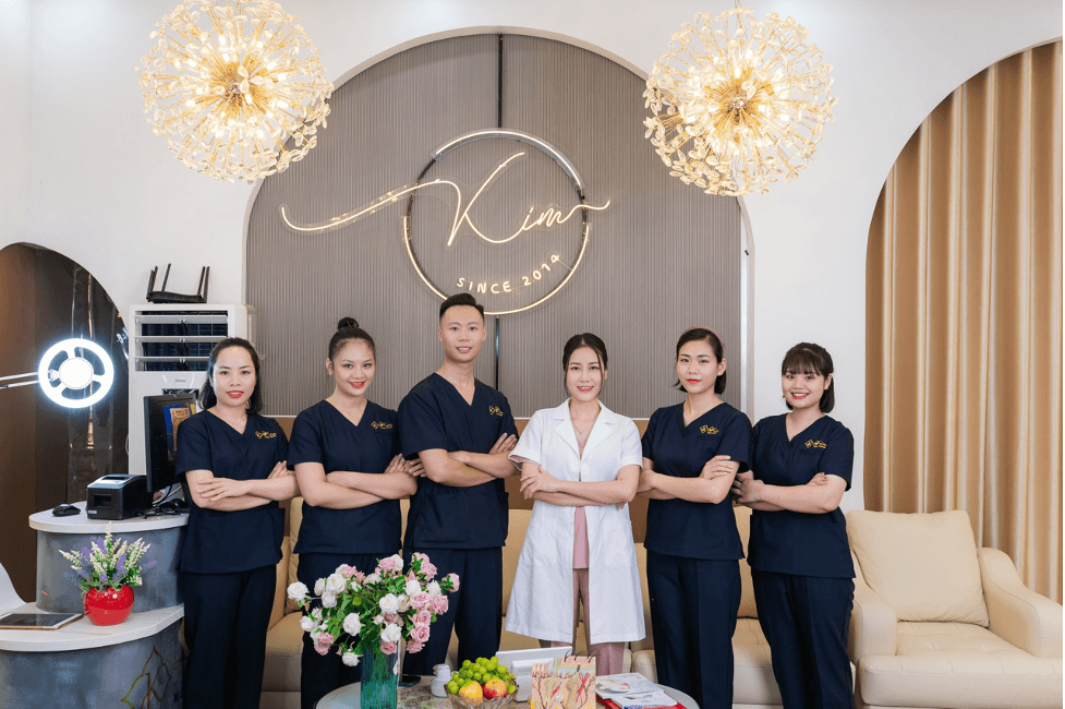 Phòng khám thẩm mỹ với nhân viên mặc đồng phục xanh, đứng tự tin trước logo với ánh sáng rực rỡ.