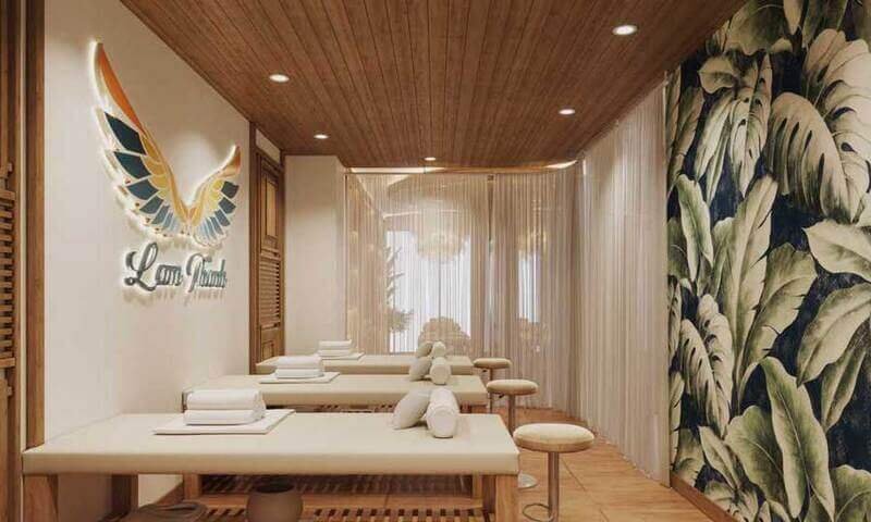 Phòng spa trang nhã với bàn massage và nội thất trang trí cây xanh, đèn chiếu sáng ấm áp và logo nổi bật trên tường.