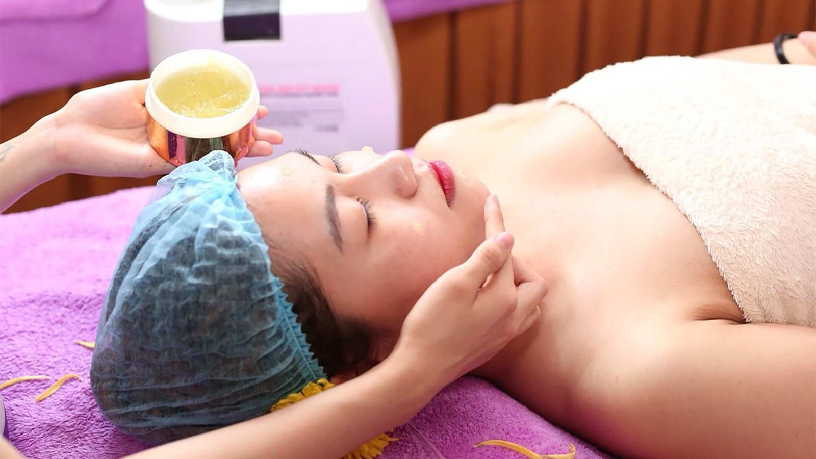 Khách hàng được massage mặt, thư giãn tại spa với khăn xanh, khăn lông và hỗn hợp dưỡng chất thiên nhiên.