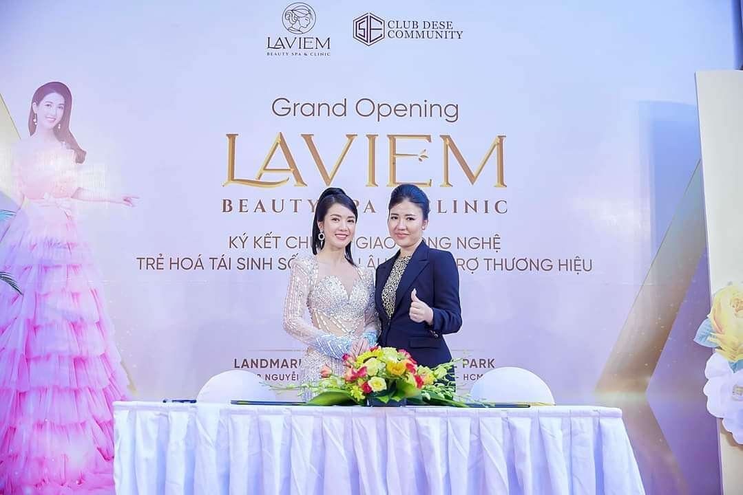 Hai người phụ nữ tại sự kiện khai trương LavieM Beauty Spa & Clinic, phía sau là logo và banner.