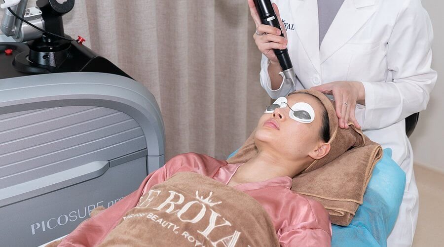 Nhân viên spa thực hiện liệu pháp laser Picosure cho khách hàng nằm trên giường, mắt đeo kính bảo hộ.