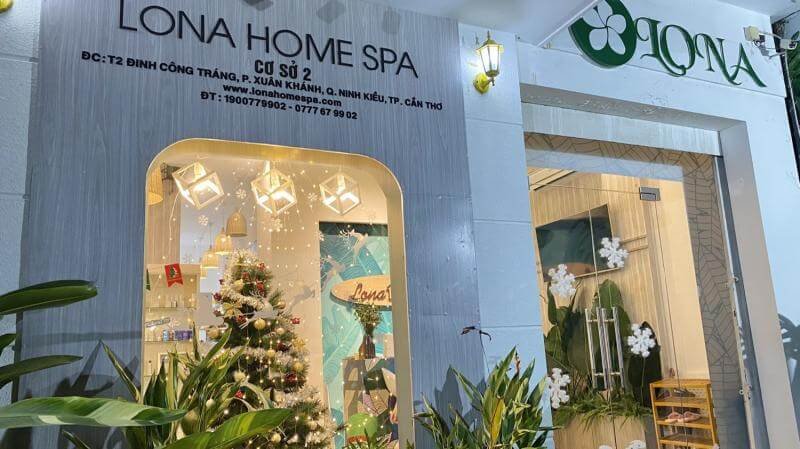 Mặt tiền của một spa với bảng hiệu và cây xanh trang trí, không gian bên trong sáng đèn và có cây thông Noel.