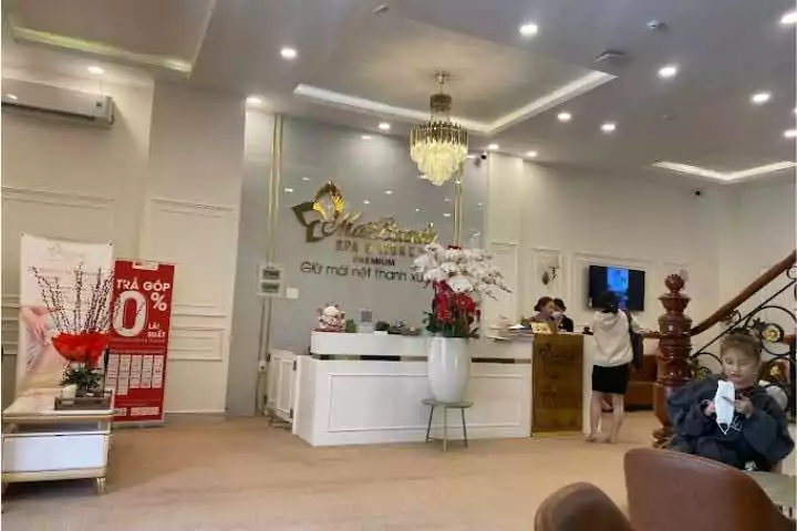 Spa cao cấp với quầy lễ tân sang trọng ánh đèn vàng, trang trí hoa tươi và bảng khuyến mãi trả góp 0% bên trái.