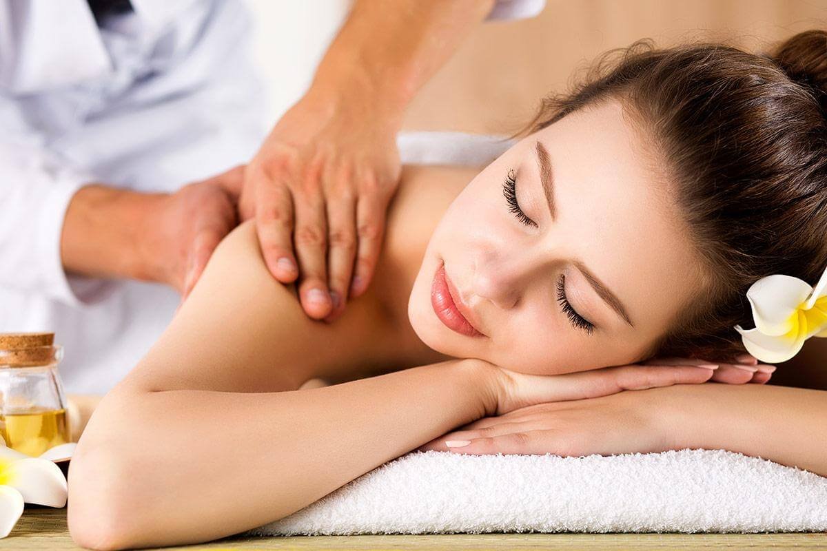 Người phụ nữ thư giãn trong liệu pháp massage, hoa plumeria và dầu thơm bên cạnh.