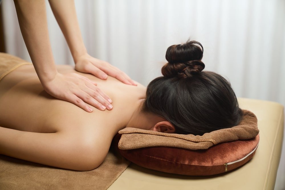 Người phụ nữ thư giãn trên giường massage, được mát-xa lưng tại spa.