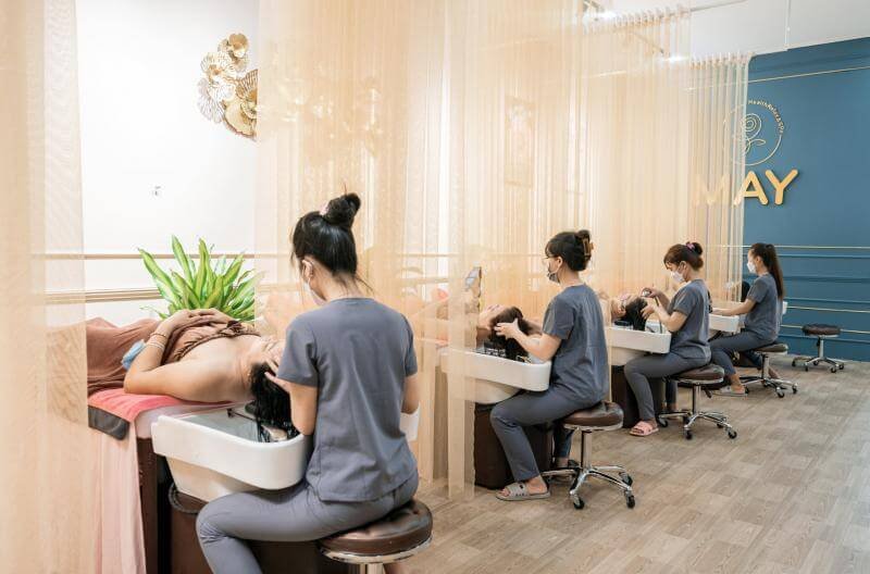 Nhân viên spa đang gội đầu cho khách hàng trong không gian nội thất trang nhã, có rèm ngăn cách từng khu vực.
