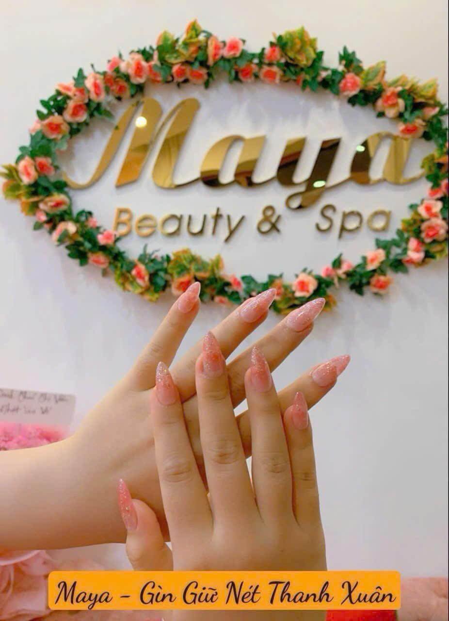 Tay với móng tay hồng lấp lánh trước biển hiệu Maya Beauty & Spa và hoa hồng trang trí.