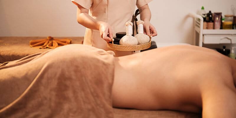 Nhân viên spa chuẩn bị massage thảo dược cho khách hàng thư giãn trên giường spa, không gian ấm áp.