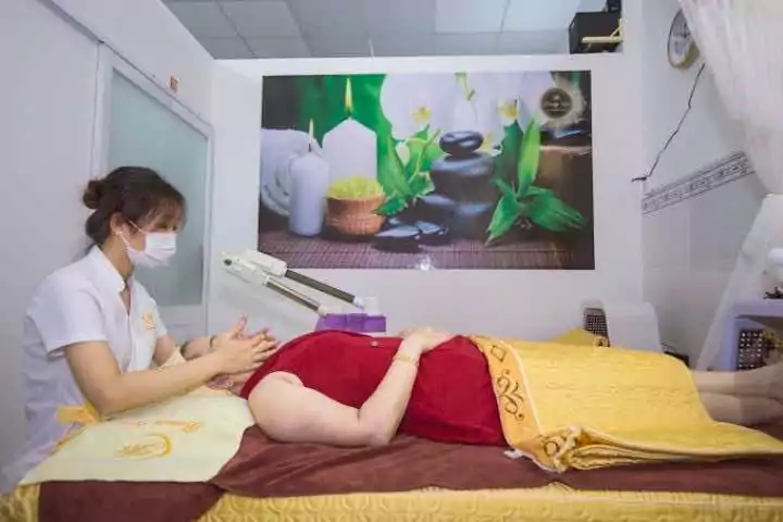 Nhân viên spa mát-xa cho khách hàng nằm thư giãn trong phòng trị liệu với ánh nến và hình ảnh thiên nhiên.