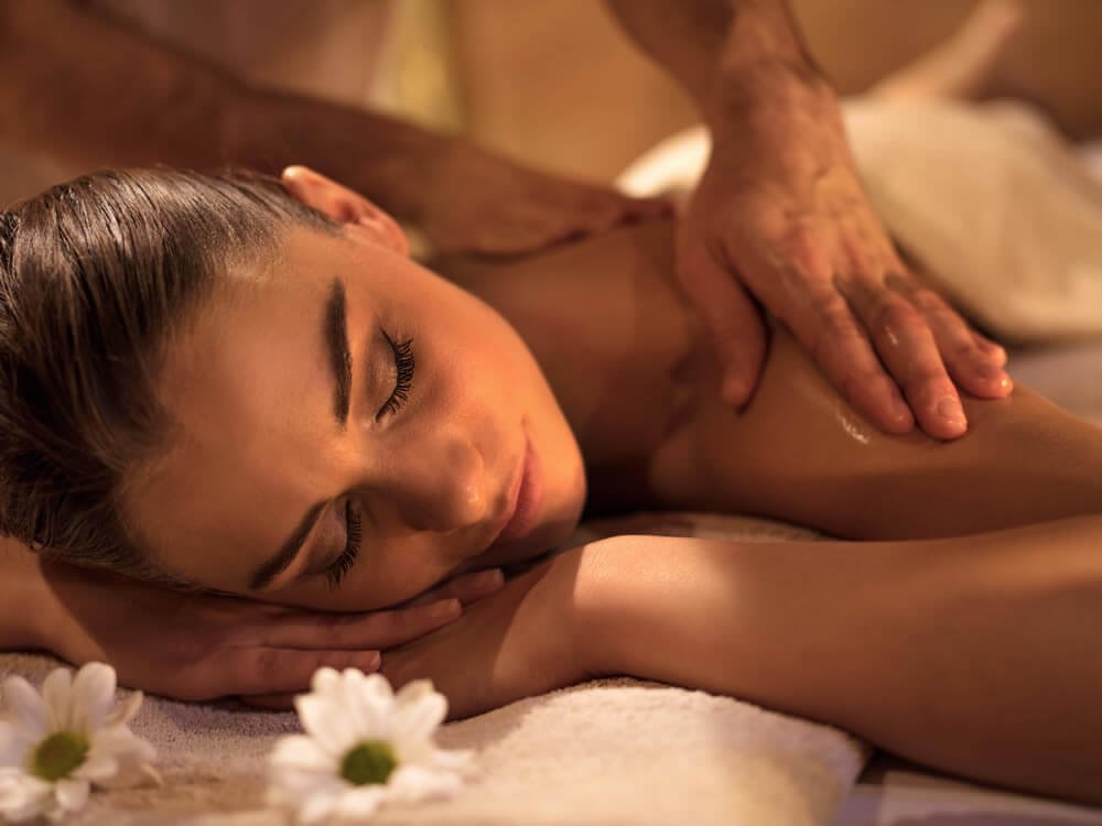 Người phụ nữ tận hưởng dịch vụ massage thư giãn tại spa với nến thơm và ánh sáng nhẹ nhàng.