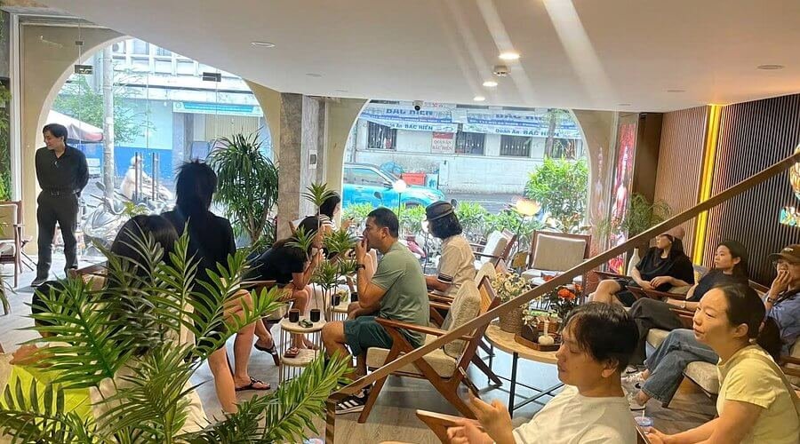 Quán cà phê đông khách với nhiều người ngồi trò chuyện thư giãn trong không gian thoải mái và xanh mát.