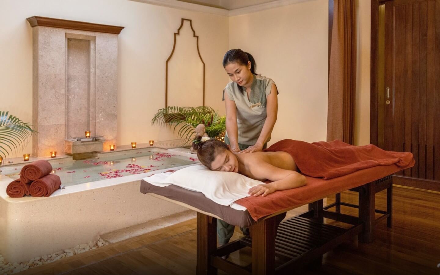 Người phụ nữ thư giãn với liệu pháp massage tại spa sang trọng cạnh bồn tắm thả hoa.