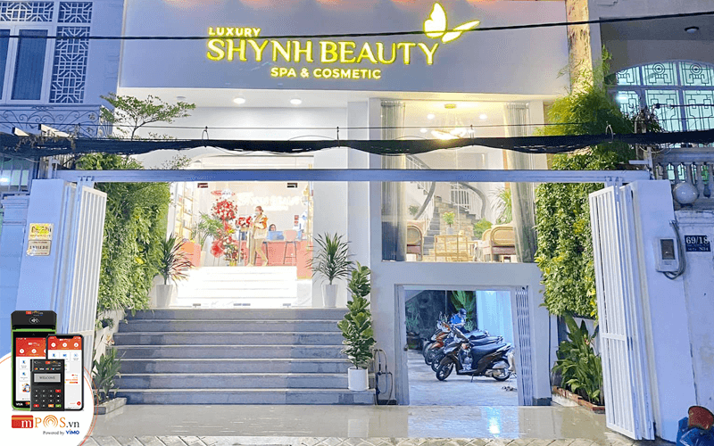 Mặt tiền của Shynh Beauty Spa & Cosmetic, trang trí hiện đại với cây xanh và bảng hiệu sáng nổi bật.