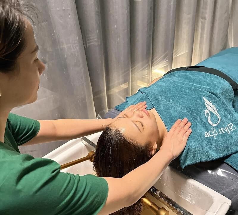 Nhân viên spa thực hiện massage mặt cho khách hàng trên bàn trị liệu có thương hiệu Sky Spa.