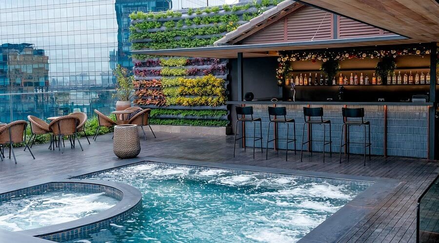 Quầy bar trên sân thượng với hồ bơi và tường cây xanh, tạo không gian thư giãn giữa trung tâm thành phố.