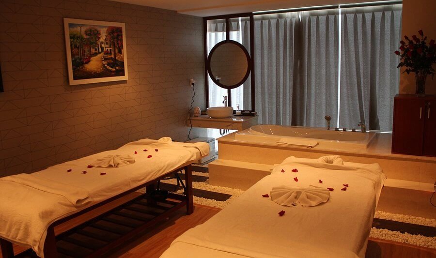 Phòng spa thư giãn với giường massage đôi, trang trí hoa hồng, bồn tắm và ánh sáng dịu nhẹ.