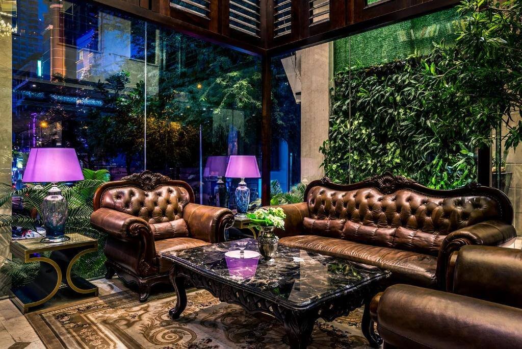 Phòng khách sang trọng với ghế sofa da nâu, bàn đá cẩm thạch, đèn bàn tím, cây xanh và cửa kính.