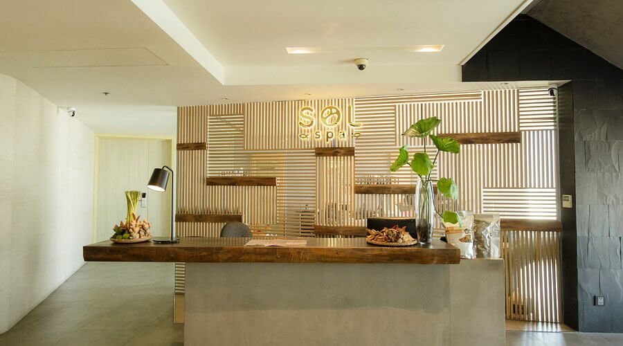 Quầy lễ tân spa hiện đại với trang trí cây xanh và bàn gỗ, tạo không gian thư giãn và sang trọng.