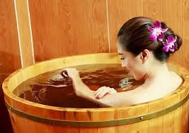 Người phụ nữ thư giãn trong thùng gỗ tắm với hoa lan trên tóc, tạo cảm giác thư thái và yên bình.