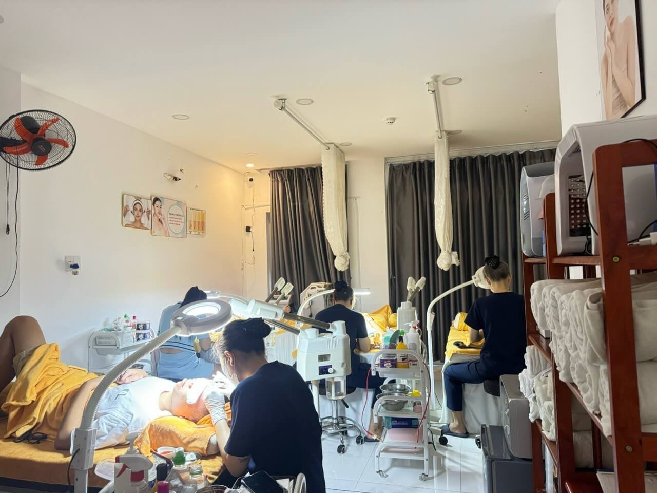 Nhân viên spa chăm sóc da mặt cho khách hàng trong phòng có thiết bị hiện đại và khăn tắm xếp gọn.gàng.