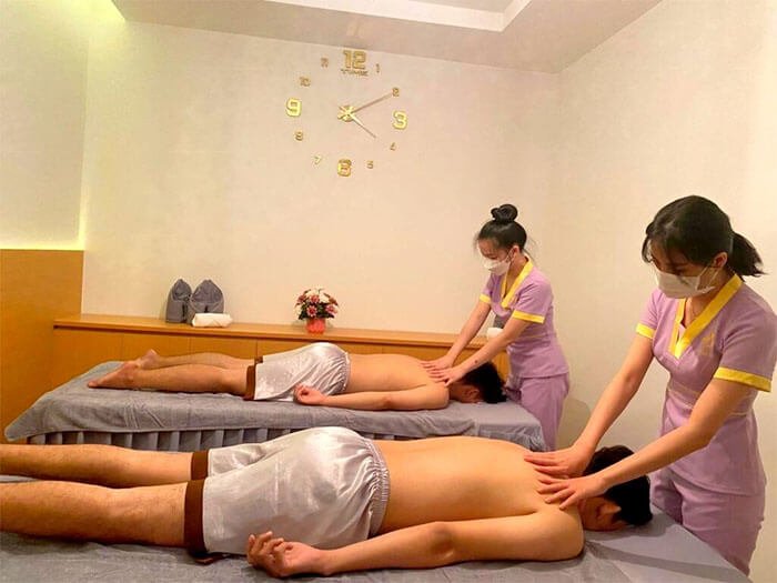 Hai nhân viên spa đang mát-xa cho hai khách hàng trong phòng thoải mái, không gian yên tĩnh với đồng hồ treo tường.