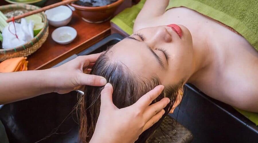 Người nằm thư giãn khi được massage da đầu trong không gian spa với khăn và dụng cụ chăm sóc.