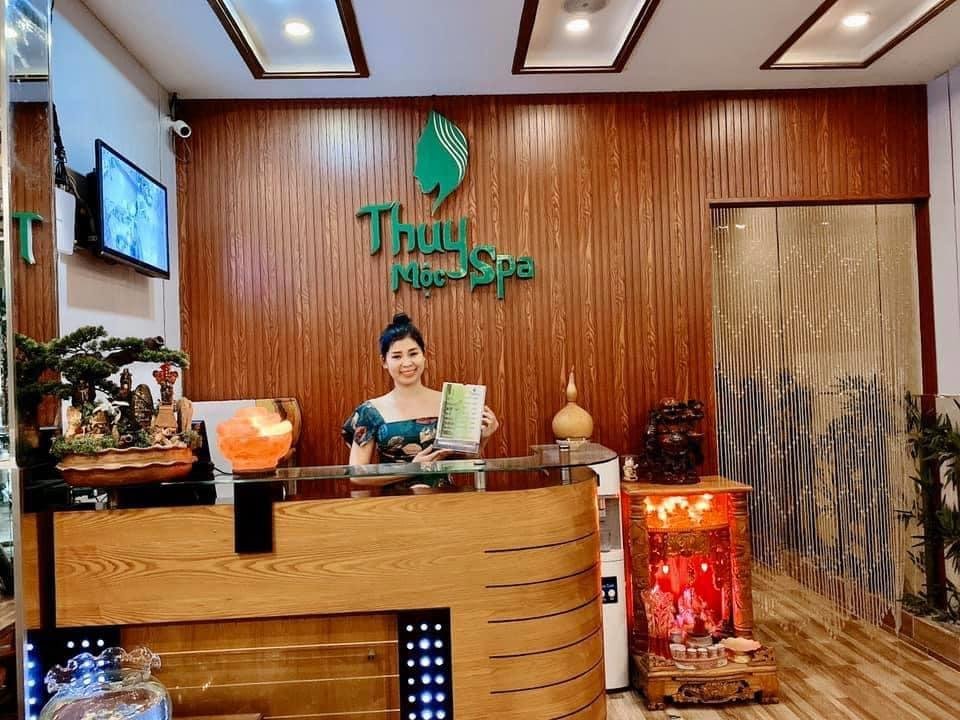 Nhân viên đứng tại quầy lễ tân Thủy Mộc Spa, môi trường ấm cúng với nội thất gỗ và ánh sáng nhẹ nhàng.