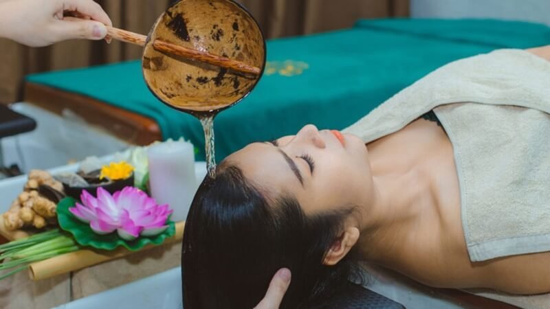 Người phụ nữ thư giãn trong liệu pháp spa với dầu thơm, hoa sen hồng bên cạnh.